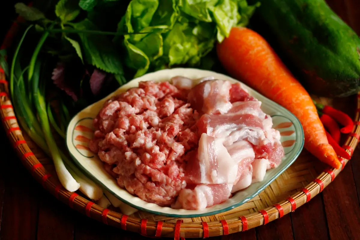 Fresh ingredients for Bun Cha including pork, herbs, and rice paper