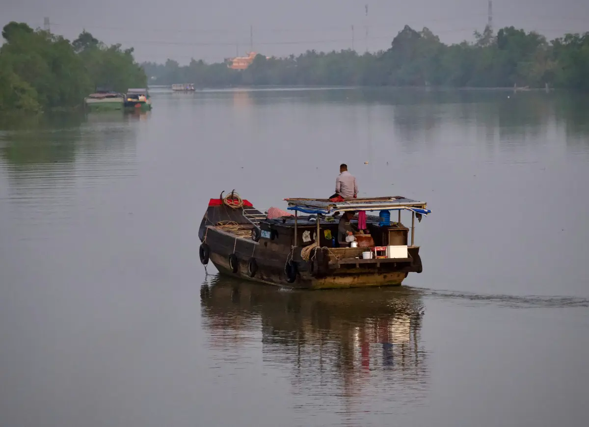 Traditional boat on Mekong Delta canal lined with palm trees